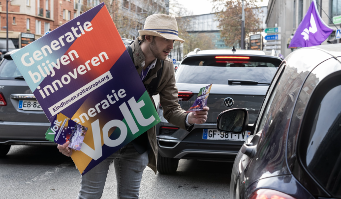 Volunteer out flyering in the streets of Paris approaches a car at a stop to hand out Volt flyer