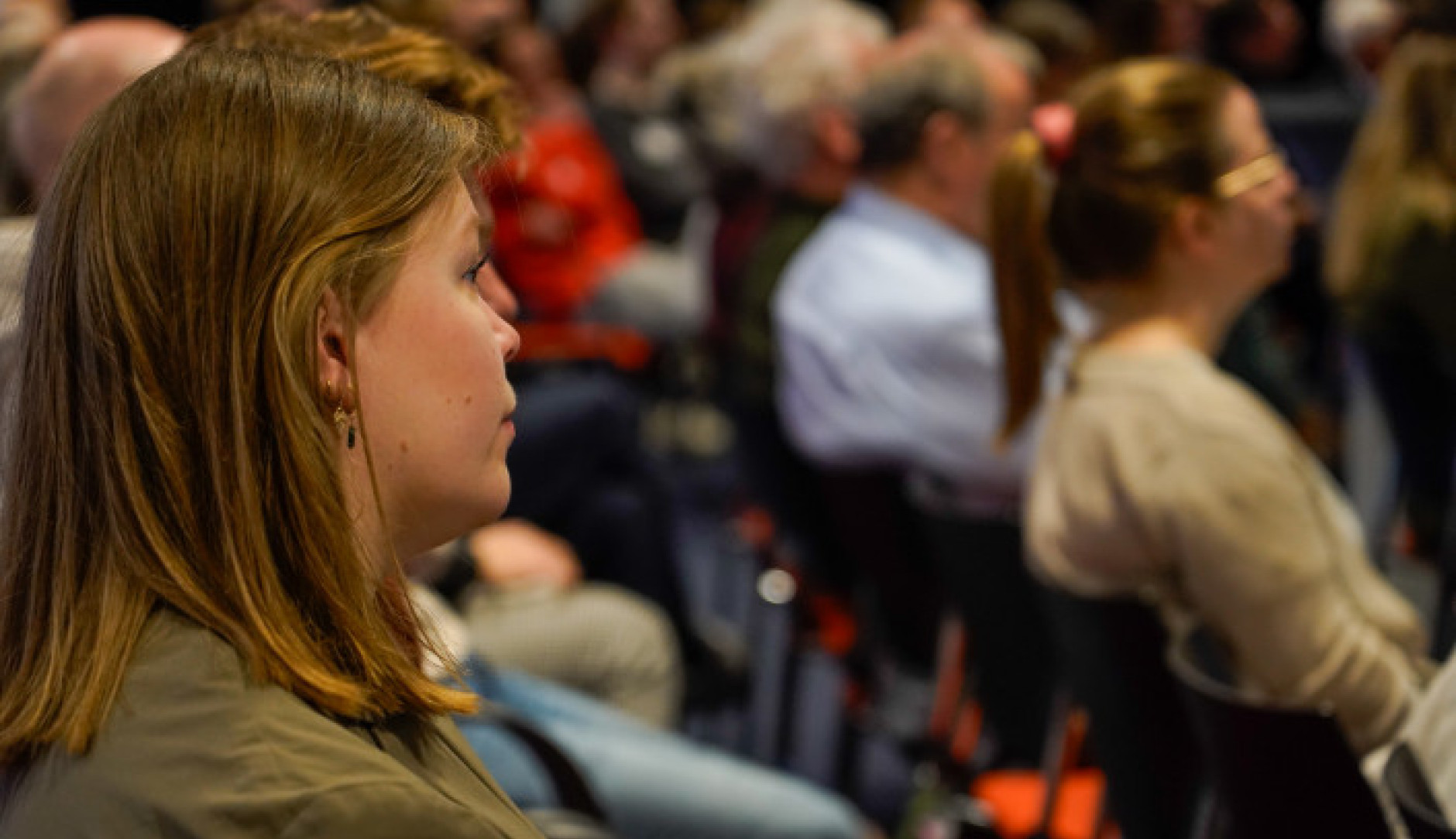Photo of people sitting on chairs in rows and listening to a presentation