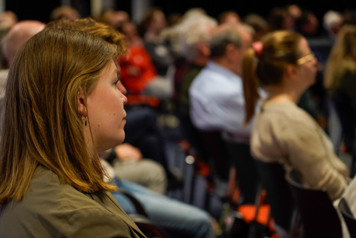 Photo of people sitting on chairs in rows and listening to a presentation