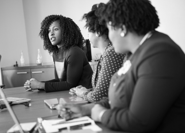 Three women sit at a boardroom table