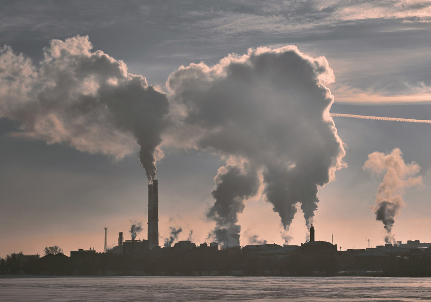 A large industrial complex with multiple smokestacks emitting thick clouds of smoke into the sky.