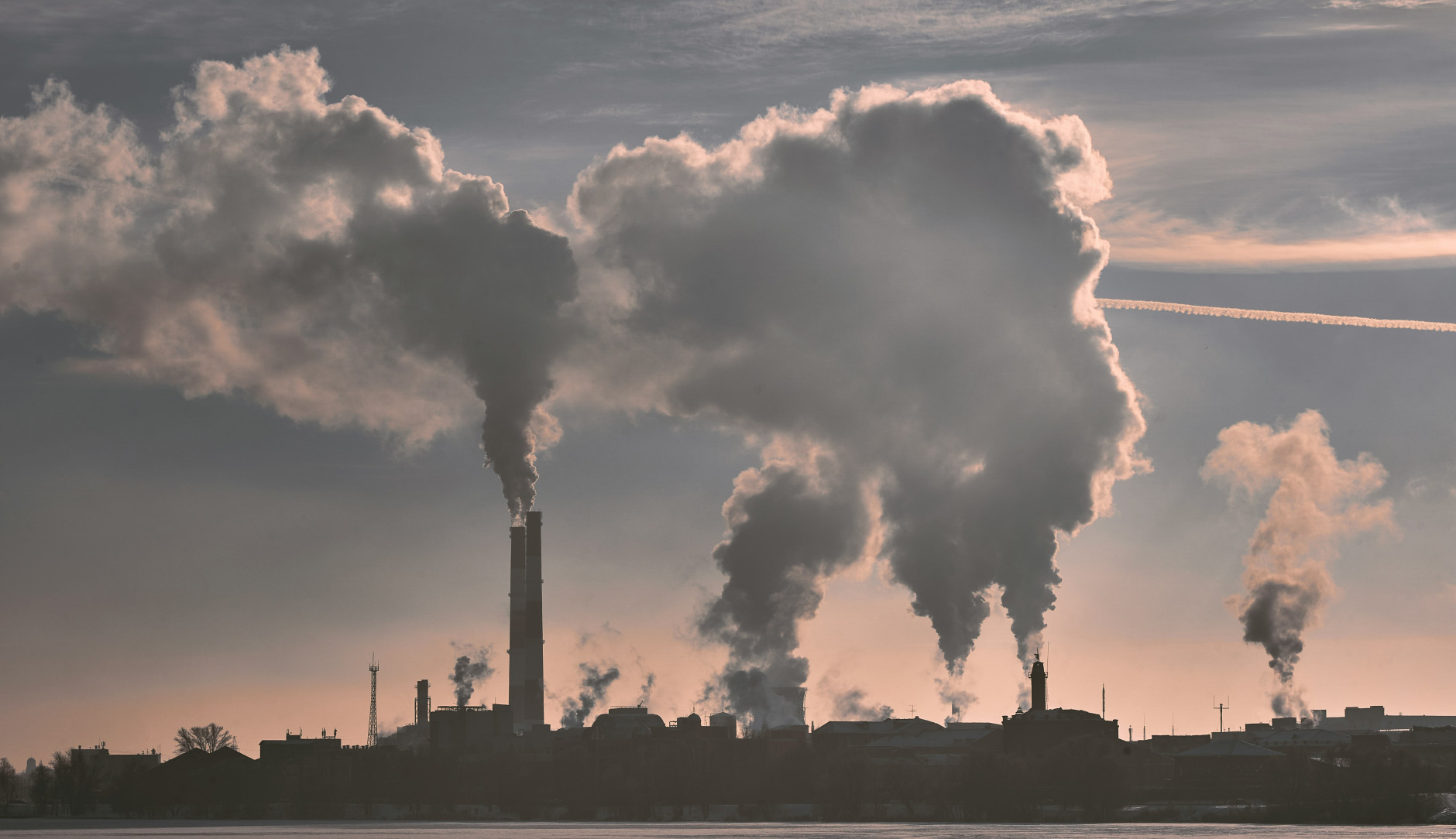 A large industrial complex with multiple smokestacks emitting thick clouds of smoke into the sky.