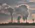 A large industrial complex with multiple smokestacks emitting thick clouds of smoke into the sky.
